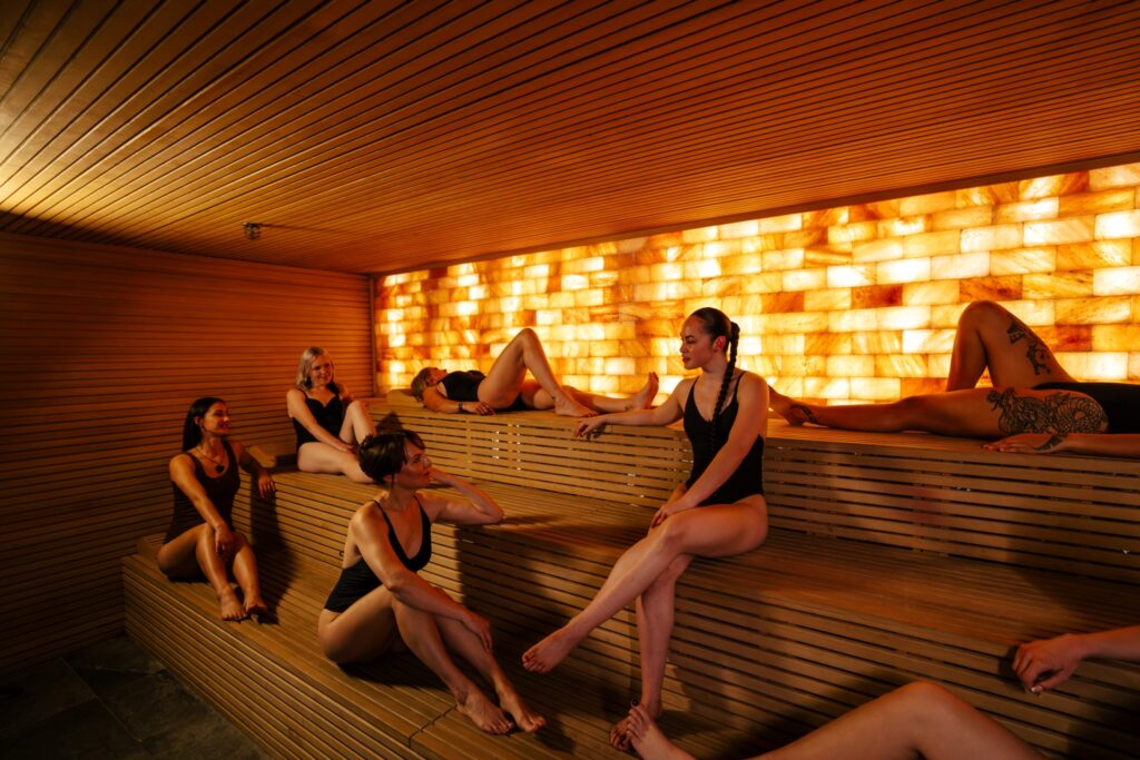 Guests relaxing together in one of the saunas along Wai Ariki's Restorative Journey, lit by a Himalayan salt wall.