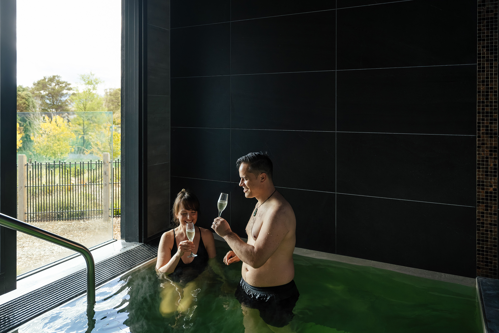Guests enjoying Puna Tūmataiti, a private geothermal pool at Wai Ariki, sharing drinks in a moment of celebration.