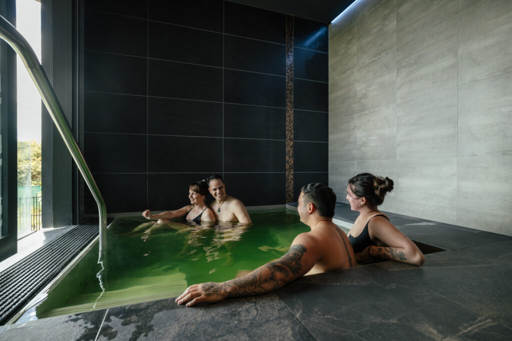 Guests enjoying Puna Tūmataiti, a private geothermal pool at Wai Ariki, sharing conversation together.