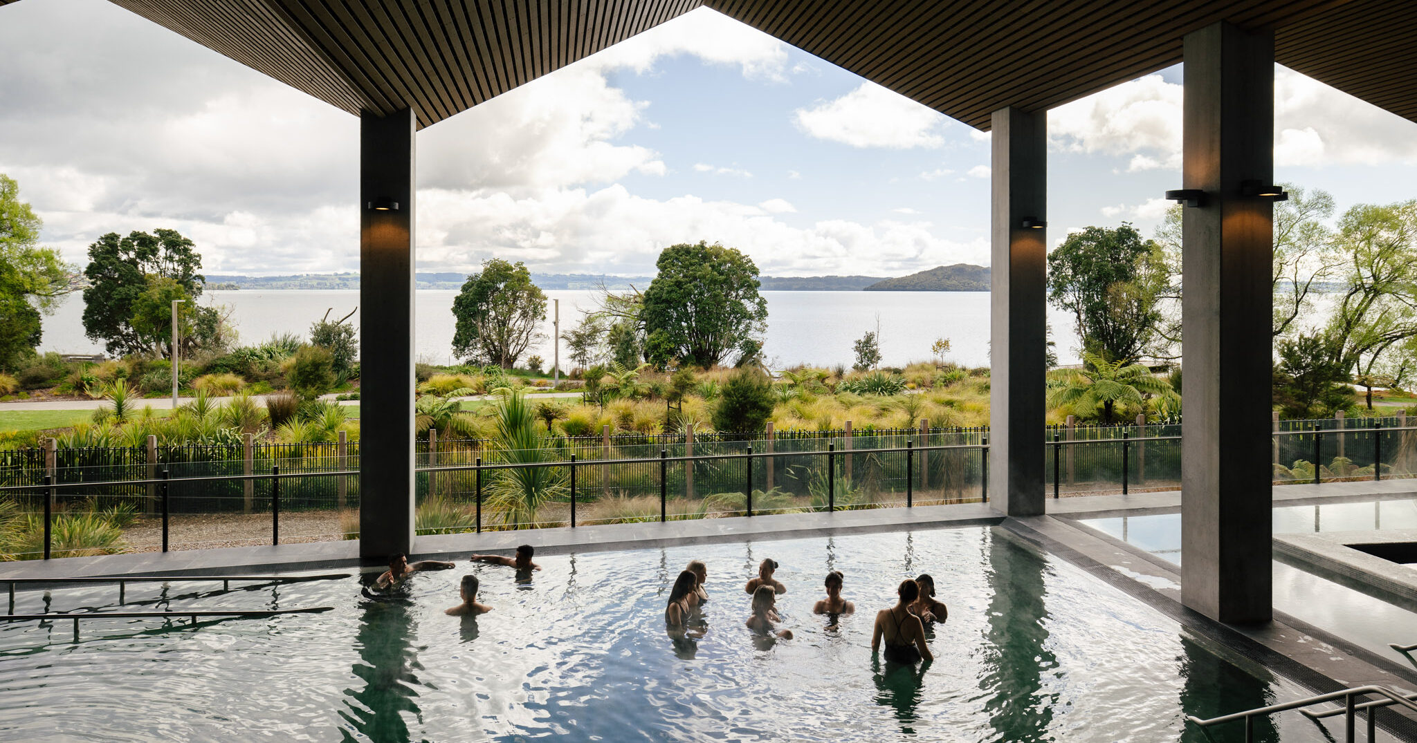 Guests bathing in Wai Ariki's outdoor restorative geothermal pool, with panoramic views of Lake Rotorua and surrounding native bush.