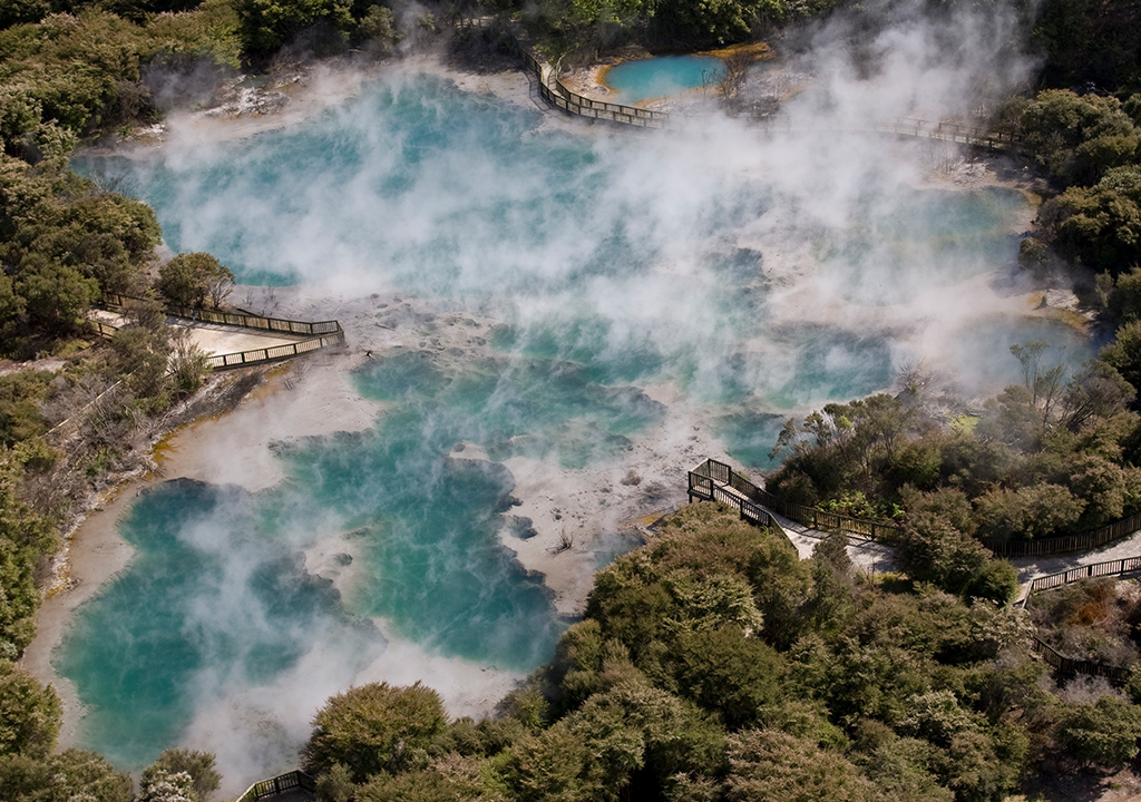 Steam rising above a vivid blue geothermal pool surrounded by native vegetation at Kuirau Park.