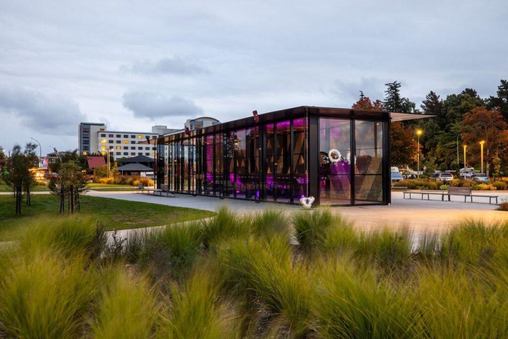 Te Arawa Whare Waka illuminated beside landscaped grounds at the Rotorua Lakefront.