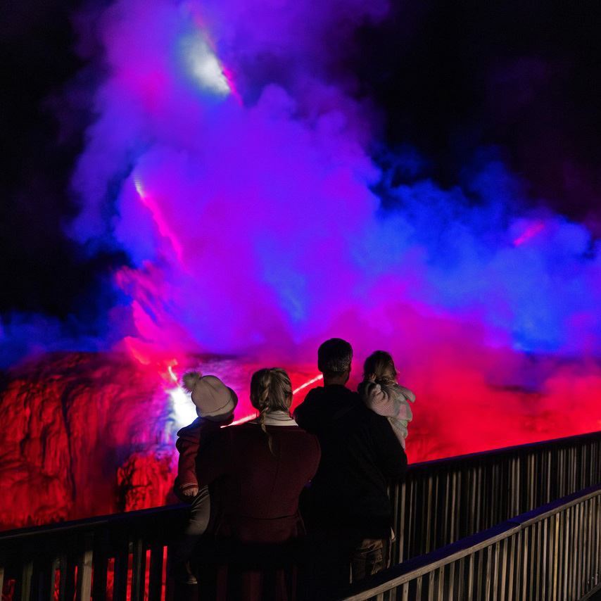 Visitors watching geothermal steam illuminated in red, purple and blue at Te Puia.