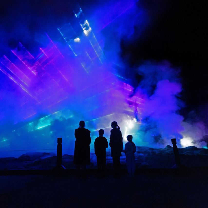 Visitors silhouetted against illuminated steam and colourful light projections at Te Puia.
