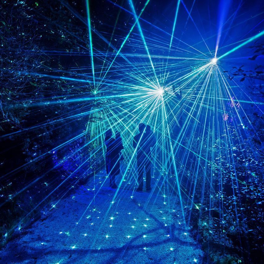 Visitors walking through blue and white laser lights on the Mārama Geyser Light Trail.