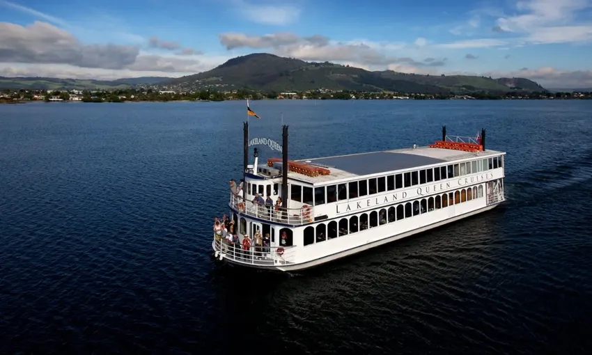 Lakeland Queen cruising across Lake Rotorua with the city and hills in the distance.