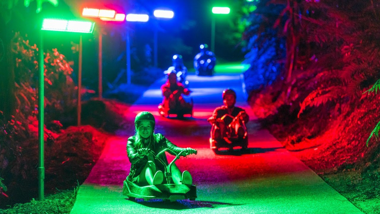 Riders travelling down the Twilight Luge track beneath red, green and blue lights.